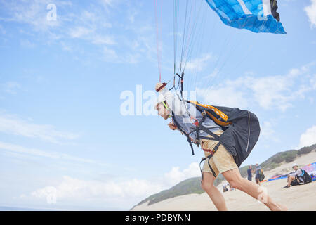 Male paraglider running with parachute on beach Stock Photo