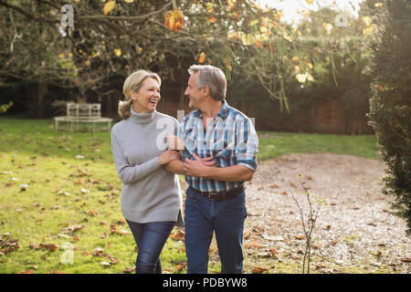 Happy, carefree mature couple walking arm in arm in sunny autumn backyard Stock Photo
