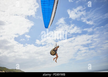 Female paraglider paragliding against sunny blue sky Stock Photo