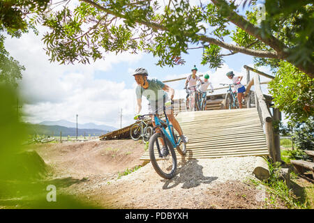 Man mountain biking down sunny obstacle course ramp Stock Photo