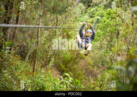 Man zip lining above trees in woods Stock Photo