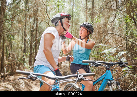 Daughter helping father with mountain biking helmet on trail in woods Stock Photo