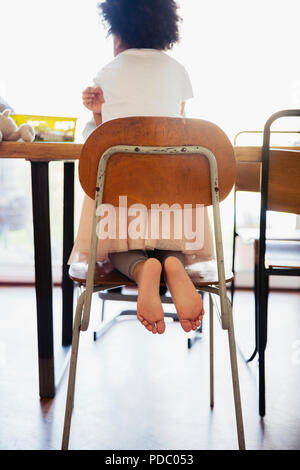 Cute, barefoot girl in tutu kneeling on dining room chair Stock Photo