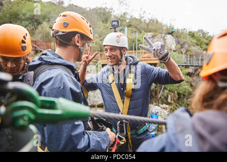 Enthusiastic man preparing to zip line, gesturing peace sign Stock Photo