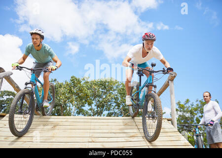 Focused men mountain biking on obstacle course ramp Stock Photo