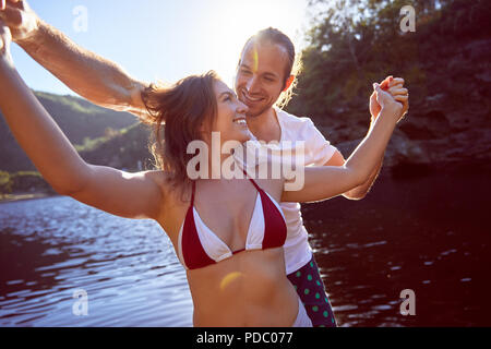 Happy, carefree couple holding hands at sunny summer lake Stock Photo