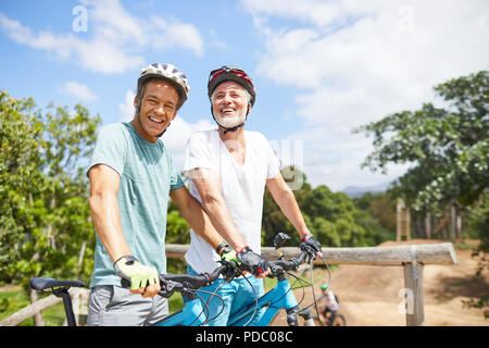 Portrait confident father and son mountain biking on sunny trail Stock Photo