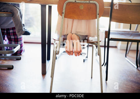 Cute, barefoot girl kneeling on dining chair Stock Photo