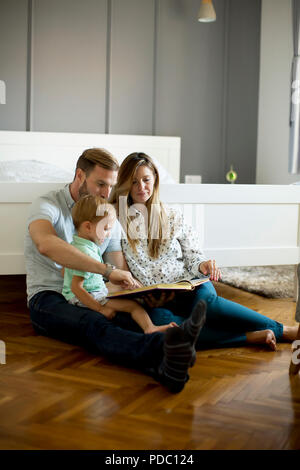 Young parents reading book to little boy and have fun on the floot in the room Stock Photo