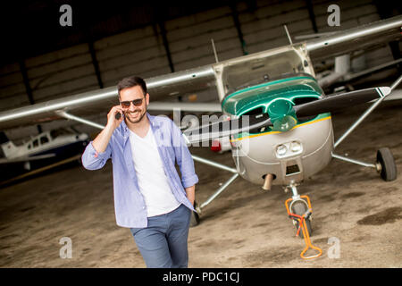 Young handsome young pilot checking airplane in the hangar and using mobile phone Stock Photo