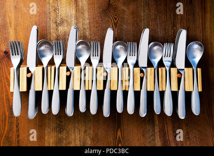 lots of knives forks and spoons staked in a line in five wooden cutlery holders on a wooden table top, color photograph Stock Photo