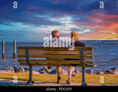 An older couple sitting on a bench by the sea Stock Photo