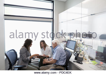 Female doctor guiding senior male patient with daughter signing paperwork in clinic office