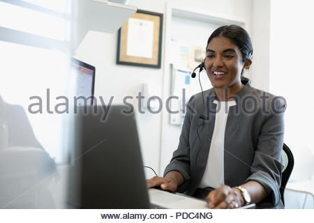 Smiling female doctor using hands-free telephone at laptop in clinic office