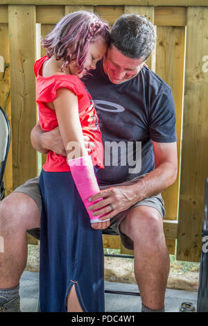 Male(uncle) sitting in chair, outside, comforting neice, who has pink cast on broken right arm. Vertical and both model released. Stock Photo