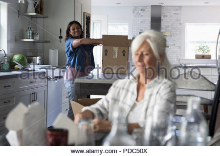 Daughter helping senior mother downsize, packing dishes in kitchen