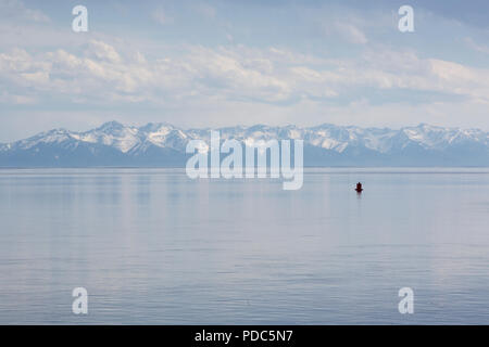 A view of the snow-capped mountains and calm waters of Baikal lake in summer, Irkutsk oblast, Russia