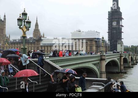 London 9th August 2018:  Crowds of tourists on Westminster Bridge shelter from the rain under umbrellas. Credit: Claire Doherty/Alamy Live News Stock Photo