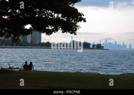 A couple watches the sun set at Promontory Point in Hyde Park with the Chicago skyline off in the distance. Stock Photo