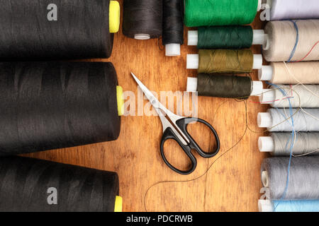 A closeup photo of sewing thread spools, beige, grey, and black, with scissors in a wooden box Stock Photo
