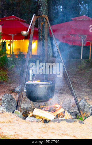 The kettle on a wooden crossbeam hangs over a fire on forest , white smoke Stock Photo