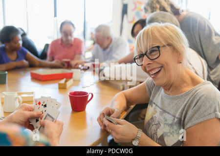 Happy senior woman playing cards with friend at table in community center Stock Photo