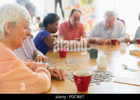 Senior woman assembling jigsaw puzzle with friends at table in community center Stock Photo