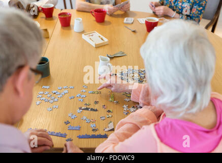 Senior friends assembling jigsaw puzzle at table in community center Stock Photo