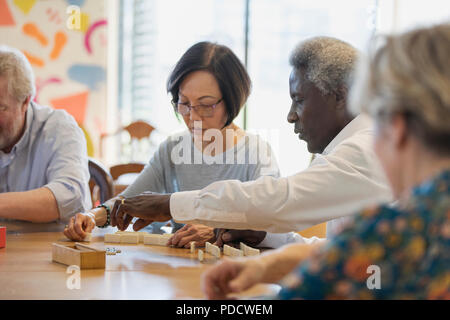 Senior friends playing mahjong at table in community center Stock Photo