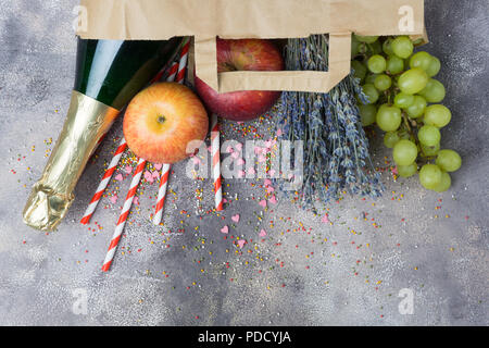 Wine, fruits, flowers (set for the party or picnic) in a paper craft pack on a gray concrete background. Top view. Stock Photo