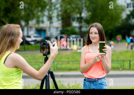 Two girls girlfriends, in summer in park in nature. In hands holding a smartphone tells about new features. Writes the video to the camera. Stock Photo