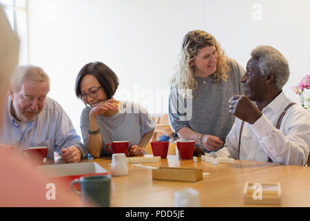 Volunteer talking with senior man playing games at table in community center Stock Photo