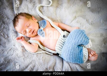 A newborn baby boy sleeping in blue and grey knitted bow tie and trousers Stock Photo
