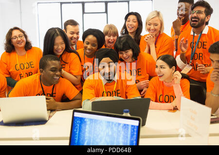 Happy hackers sharing laptop, coding for charity at hackathon Stock Photo