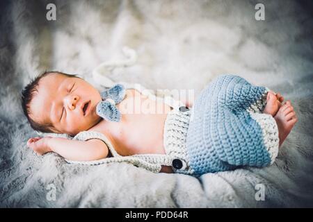 A newborn baby boy sleeping in blue and grey knitted bow tie and trousers Stock Photo