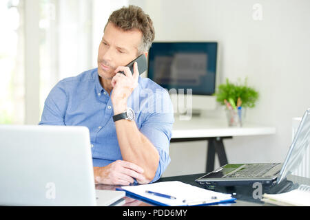 Portrait of middle aged businessman wearing shirt while sitting at the office and working. Professional man using his mobile phone and talking with so Stock Photo
