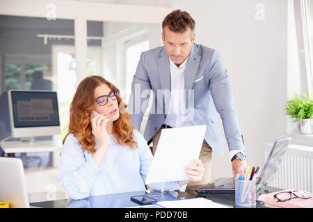Investment advisor businesswoman holding document in her hand and making call while middle aged businessman standing next to her. Stock Photo