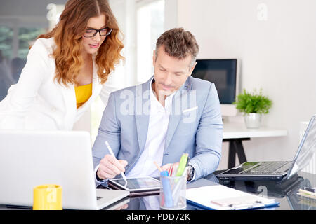 Middle aged businessman using digital tablet while working together financial assistant businesswoman. Stock Photo