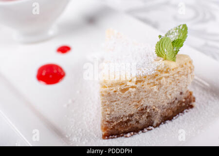 Slice of plain New York cheesecake with berry sauce decorated with mint leaf on a plate. Sweet dessert in the restaurant. Morning light Stock Photo