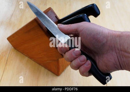 A hand holding a knife taken from a knife block and the thumb pressing on the blade to test its sharpness. It's not the sharpest knife in the block. Stock Photo