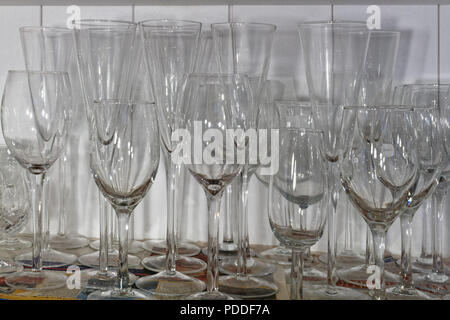 Wine glasses of various shapes and sizes standing on a sheet of newspaper on a cupboard shelf Stock Photo