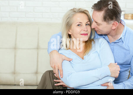 Closeup photo of cheerful excited happy happily happy with toothy shining smile blond attractive woman and man, he hugs her from behind and kisses Stock Photo