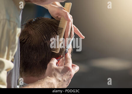 Hands of a hairdresser close-up of scissors and a comb. The barber is cutting a man and doing a haircut. Horizontal photo with text place
