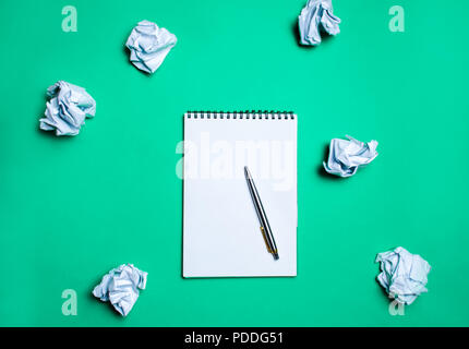 white notebook with pen on a green background among paper balls. The concept of generating ideas, inventing new ideas. Paper balls are all around. Sea Stock Photo