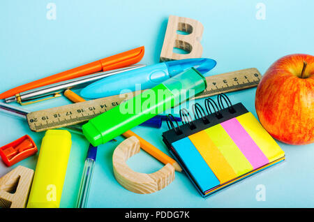 letters, apple, ruler, pens, scissors, colored markers, pencils, sticky stickers, sharpener on the school desk. back to school. blue background. place Stock Photo