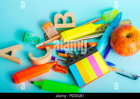 letters, apple, ruler, pens, scissors, colored markers, pencils, sticky stickers, sharpener on the school desk. back to school. blue background. place Stock Photo