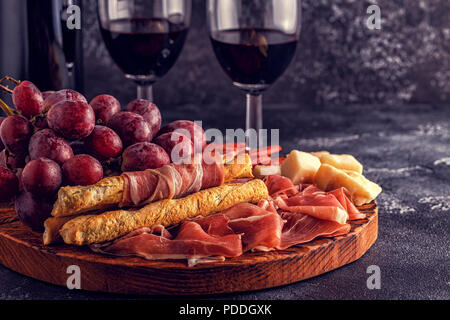 Prosciutto, sausage, wine, grape, parmesan on dark table, selective focus. Stock Photo