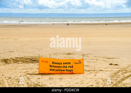 Large yellow RNLI water safety banner advising people to swim between the red and yellow flags Stock Photo