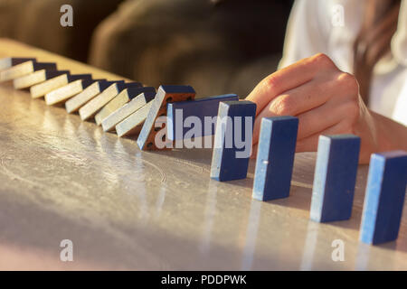 Businesswoman hand trying to stop toppling dominoes on table, strategy and successful intervention concept for business. Stock Photo