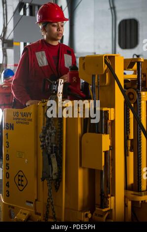 WATERS SOUTH OF JAPAN (May 15, 2018) Aviation Ordnanceman 3rd Class Jazmine Reynolds, from El Paso, Texas, moves ordnance in the hangar bay aboard the Navy's forward-deployed aircraft carrier, USS Ronald Reagan (CVN 76), as part of a replenishment-at-sea with Military Sealift Command (MSC) dry cargo/ammunition ship USNS Cesar Chavez (T-AKE 14), during sea trials. The non-combatant, civilian-crewed ship, operated by MSC, provides fuel, food, ordnance, spare parts, mail and other supplies to Navy ships throughout the world. Ronald Reagan, the flagship of Carrier Strike Group 5, provides a combat Stock Photo